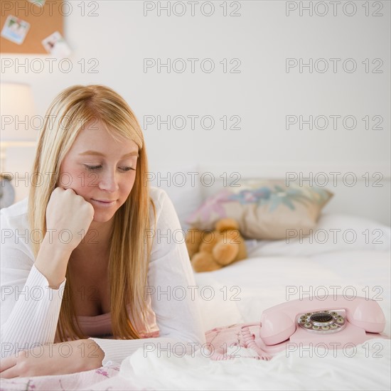 Woman lying on bed and looking at telephone. Photo : Jamie Grill Photography