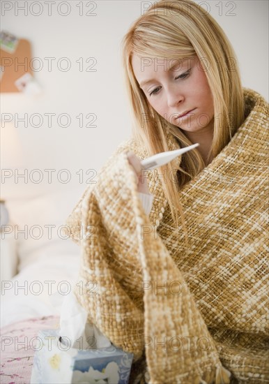 Woman wrapped in blanket measuring temperature. Photo : Jamie Grill Photography