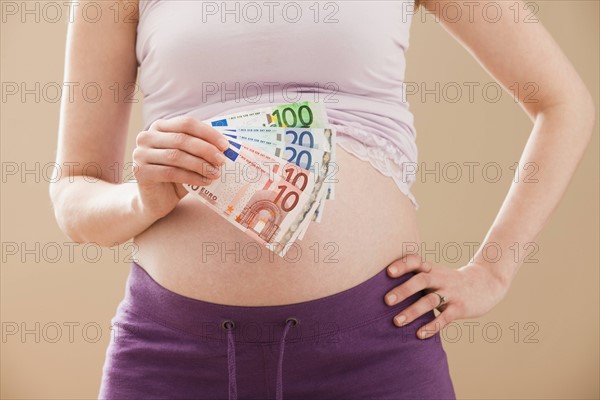 Young pregnant woman holding money roll of Euros. Photo : Mike Kemp