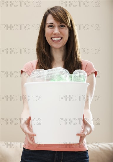 Studio portrait of smiling woman holding recycling bin in plastic bottle. Photo : Mike Kemp