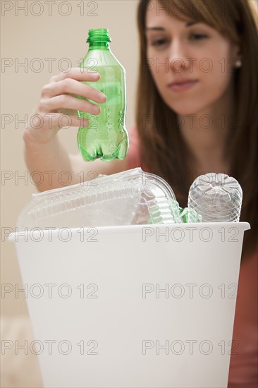 Studio shot of woman (8-9) placing plastic bottle in recycling bin. Photo : Mike Kemp