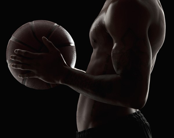 Studio shot of shirtless man holding basketball, mid section. Photo: Mike Kemp