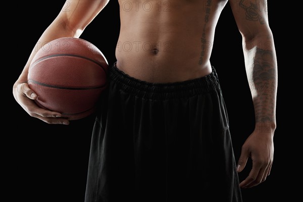 Studio shot of shirtless man holding basketball, mid section. Photo: Mike Kemp