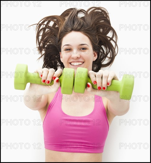 Studio portrait of young woman holding hand weights. Photo: Mike Kemp