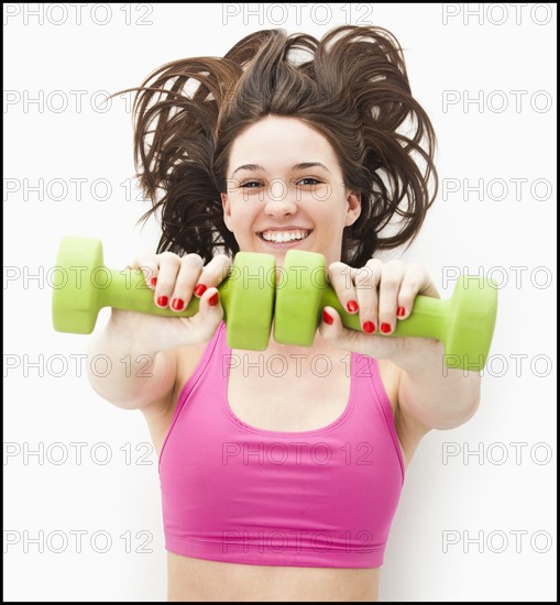 Studio portrait of young woman holding hand weights. Photo : Mike Kemp