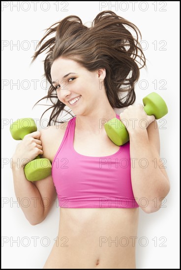 Studio portrait of young woman holding hand weights. Photo : Mike Kemp