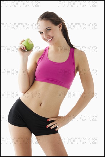 Studio portrait of young woman eating apple. Photo : Mike Kemp