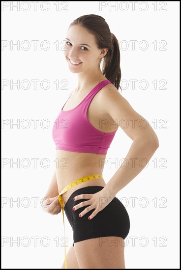 Studio portrait of young woman measuring waist. Photo : Mike Kemp