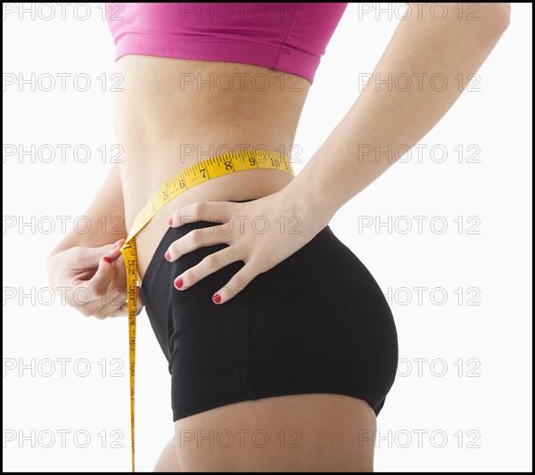 Young woman measuring waist. Photo : Mike Kemp