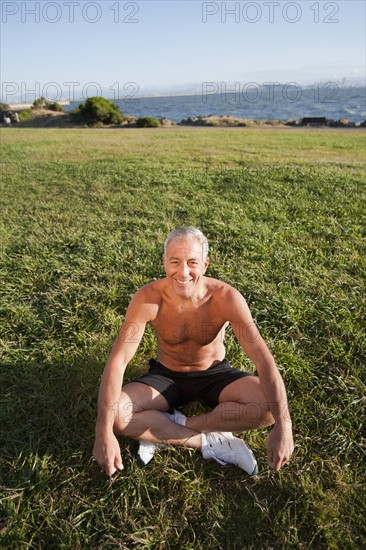 USA, California, Berkeley, Senior man sitting cross-legged on grass. Photo: Noah Clayton