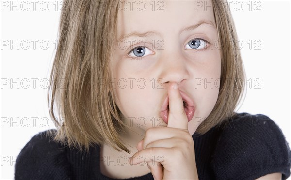 Studio portrait of girl (6-7) with finger on lips. Photo : Justin Paget