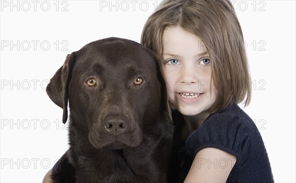 Studio portrait of smiling girl (6-7) hugging chocolate labrador. Photo : Justin Paget