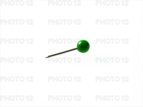 Green push pin on white background. Photo : David Arky