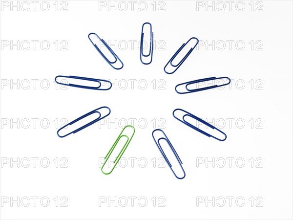 Blue and green paper clips on white background. Photo : David Arky