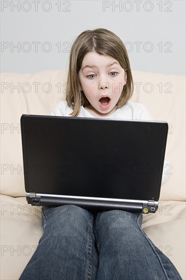 Girl (6-7) with laptop sitting on sofa. Photo : Justin Paget