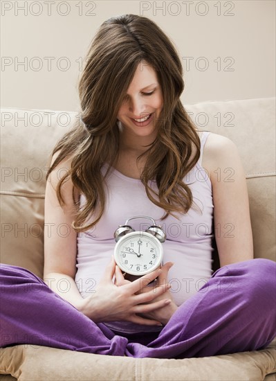 Young pregnant woman holding alarm clock. Photo : Mike Kemp