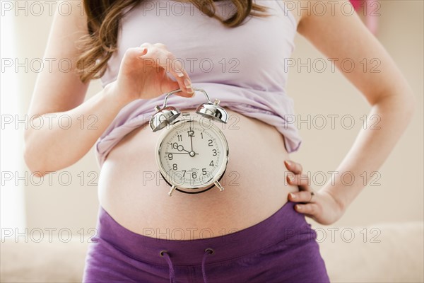 Young pregnant woman holding alarm clock. Photo : Mike Kemp