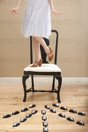 Young woman standing on chair, evading computer mice. Photo: Mike Kemp