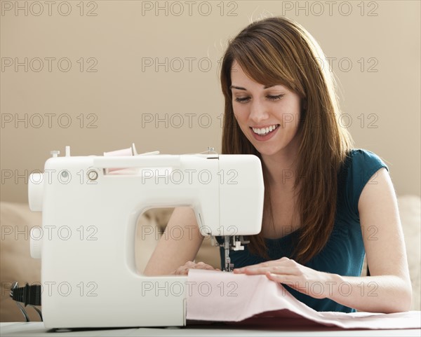 Smiling young woman using sewing machine. Photo : Mike Kemp