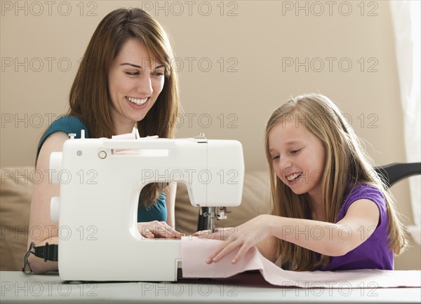 Girl (8-9) and young woman using sewing machine. Photo : Mike Kemp