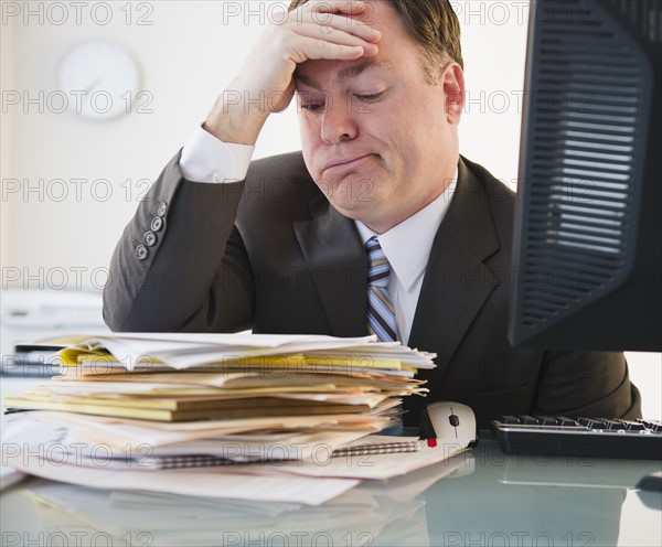 Businessman looking at stack of folders. Photo: Jamie Grill Photography