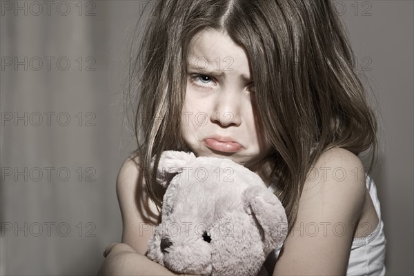Studio portrait of sad girl (6-7) with pink teddy bear. Photo : Justin Paget