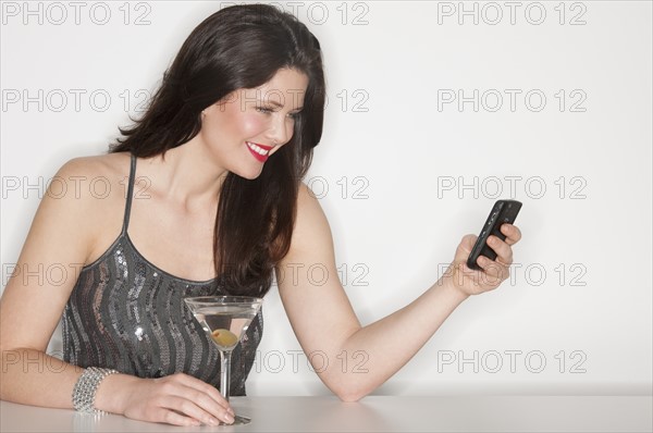 Young woman in evening wear text messaging and drinking martini.