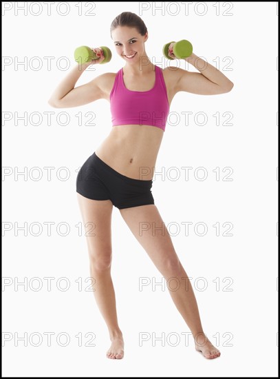 Studio portrait of young woman exercising with hand weights. Photo : Mike Kemp