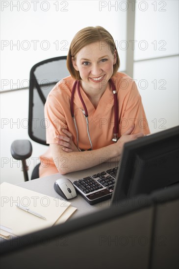 Female nurse sitting at desk and smiling.