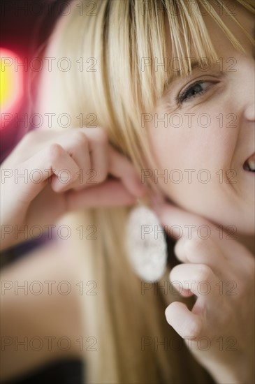 Young woman putting on earring. Photo : Jamie Grill Photography