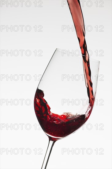 Close up of red wine being poured into glass on white background.