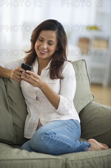 Smiling woman sitting on sofa and texting on mobile phone.