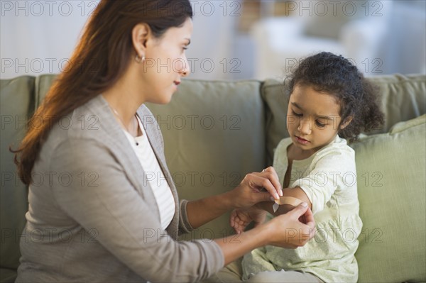 Mother applying band aid on daughter's (6-7) arm.