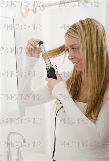 Woman doing hairstyle and using curling iron. Photo : Jamie Grill Photography