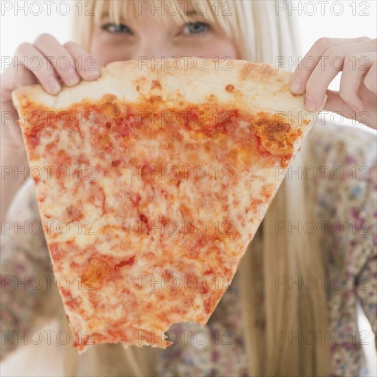 Young woman holding pizza slice. Photo : Jamie Grill Photography