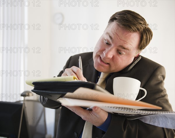 Businessman writing and talking on phone. Photo : Jamie Grill Photography