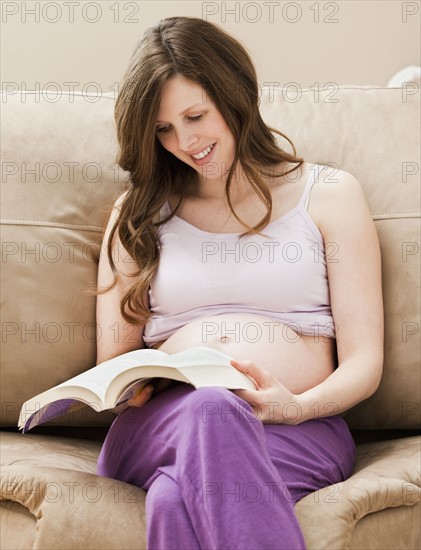 Young pregnant woman sitting on sofa, reading book. Photo: Mike Kemp