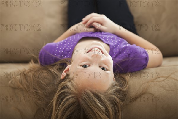Portrait of girl (8-9) lying on sofa. Photo: Mike Kemp