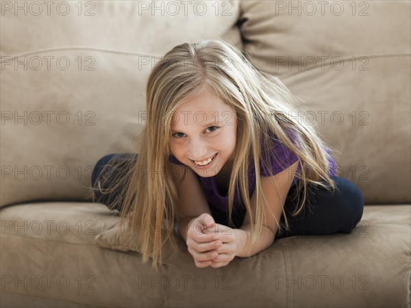 Portrait of girl (8-9) sitting on sofa. Photo: Mike Kemp