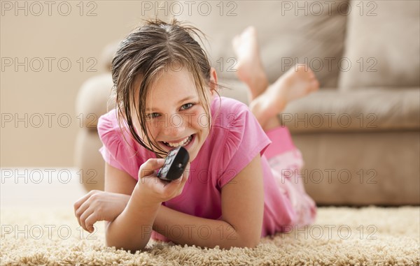 Portrait of girl (10-11) lying on floor holding remote control. Photo : Mike Kemp