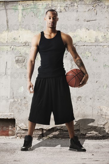 USA, Utah, Salt Lake City, Portrait of young man with basketball against dilapidated wall. Photo: Mike Kemp