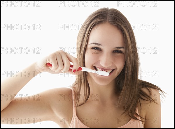 Studio portrait of young woman brushing teeth. Photo : Mike Kemp