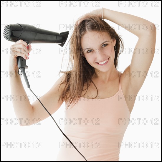 Studio portrait of young woman blow drying hair. Photo: Mike Kemp