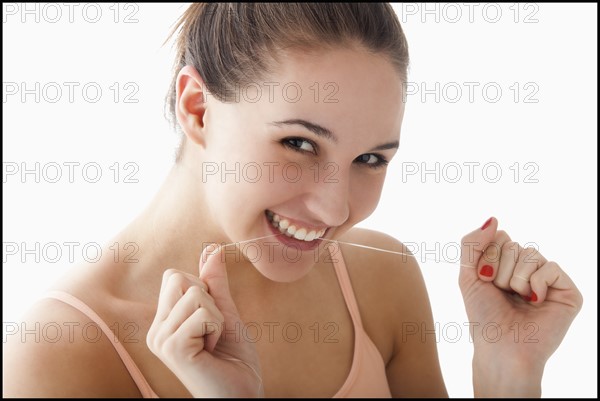 Studio portrait of young woman flossing teeth. Photo : Mike Kemp