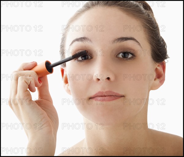 Studio portrait of young woman applying mascara. Photo : Mike Kemp