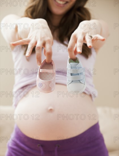 Young pregnant woman showing two different baby shoes. Photo : Mike Kemp