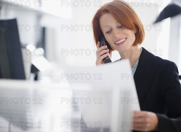 Businesswoman reading documents and talking on telephone. Photo : Jamie Grill Photography