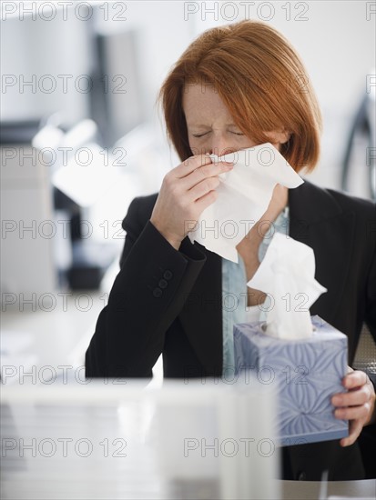 Businesswoman blowing nose. Photo : Jamie Grill Photography