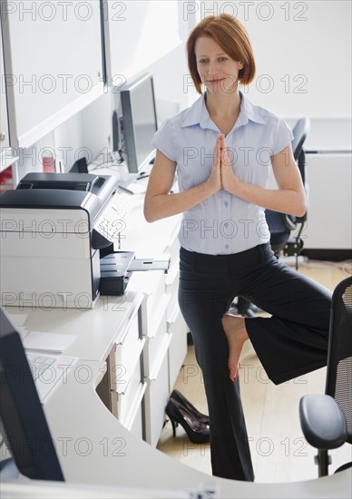 Businesswoman doing yoga position in office. Photo : Jamie Grill Photography