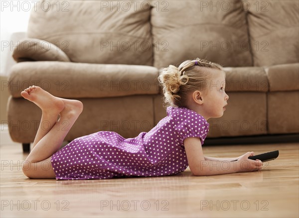 Girl (2-3) lying on floor, watching TV. Photo : Mike Kemp